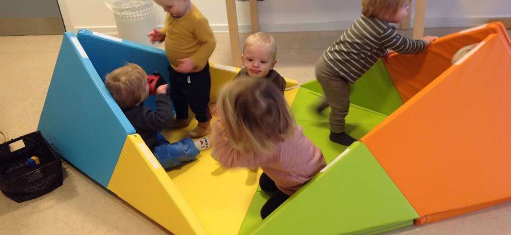 Fem børn leger på gulvet, i madras-skib.